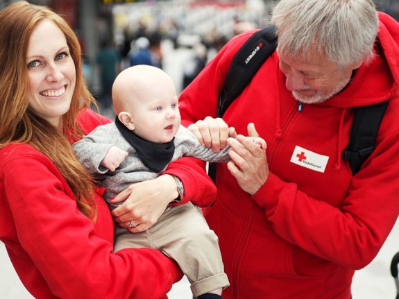 Två rödakorsare med en baby i famnen.