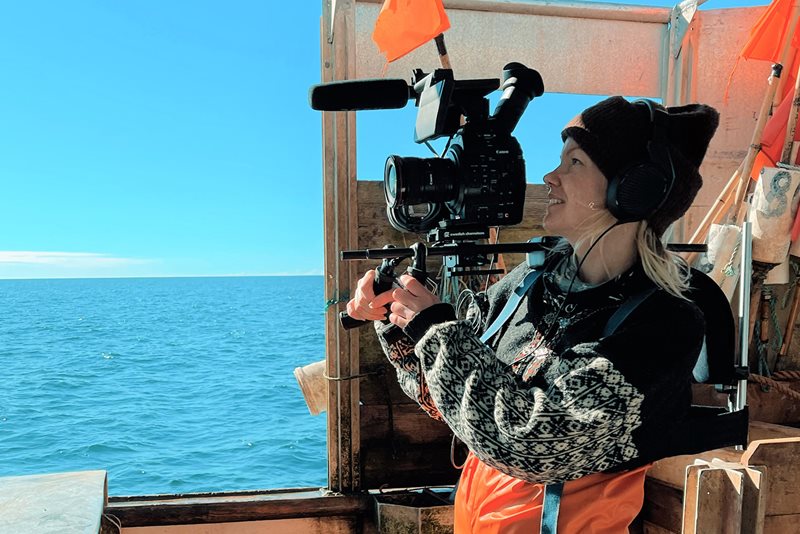 Tjej på båt filmar ut över havet med stor filmkamera.