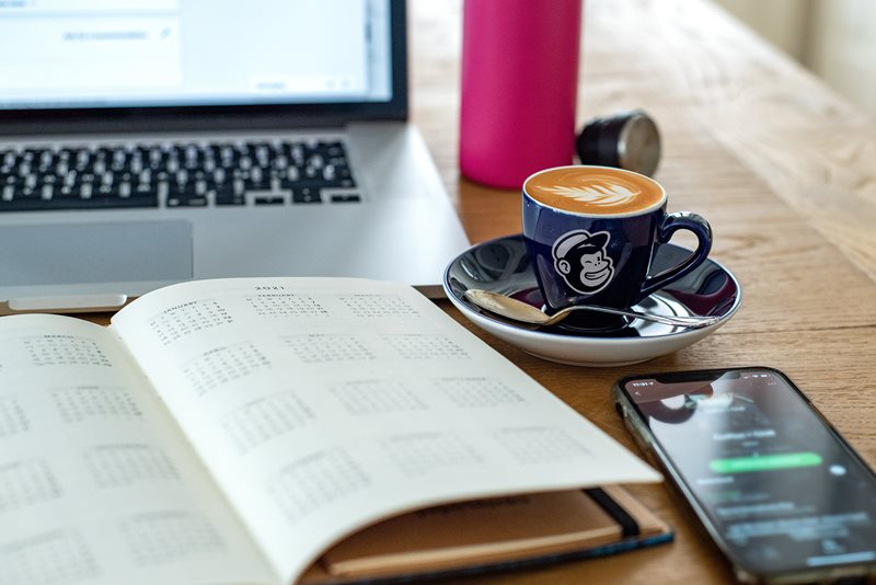En laptop, kaffekopp, kalender och mobil på ett bord