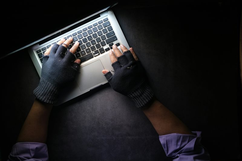 Bild på en bärbar dator och två händer med avklippta handskar på sig över tangentbordet